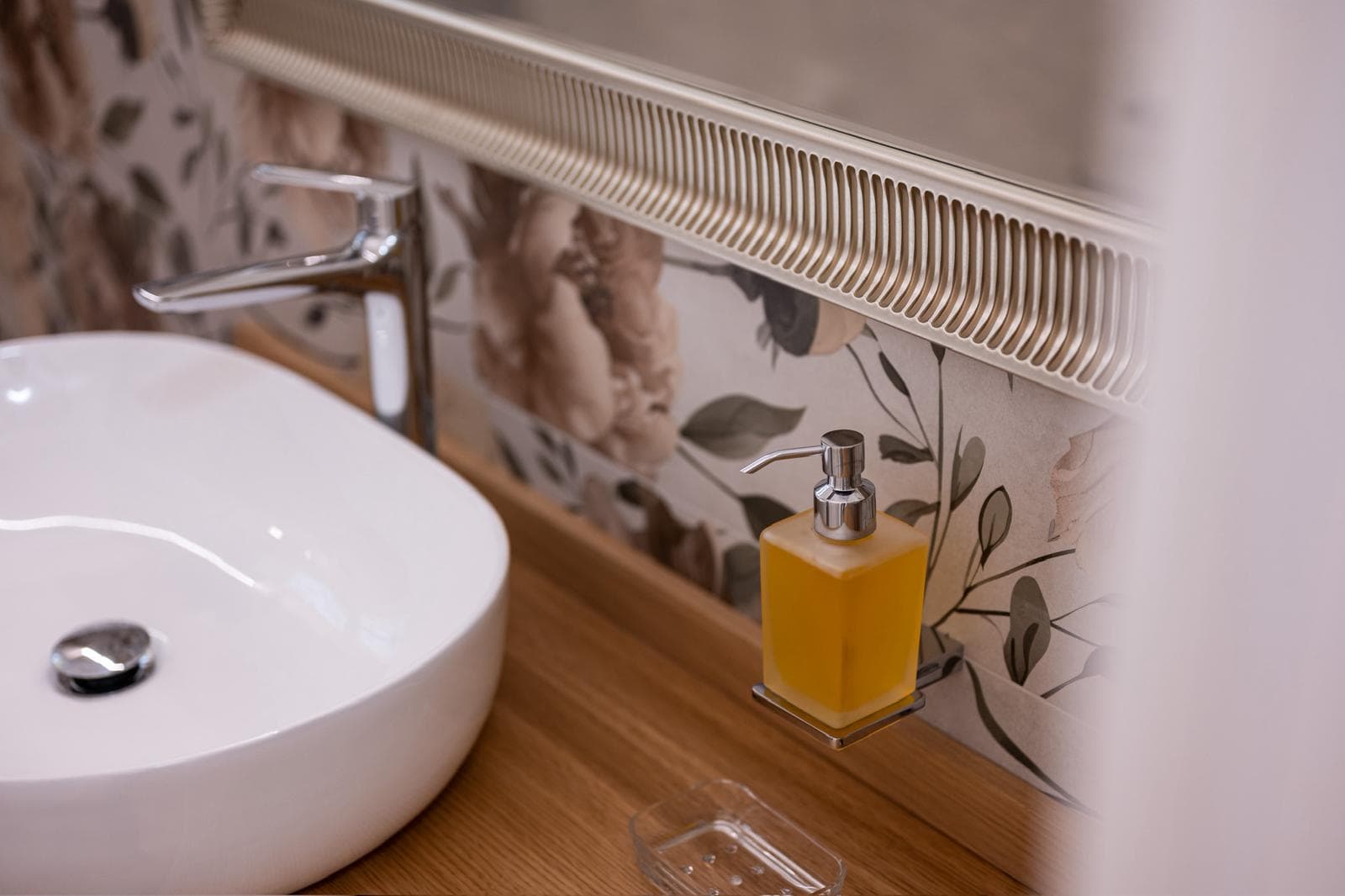 White vessel sink on wooden counter with yellow soap dispenser against elegant floral wallpaper.