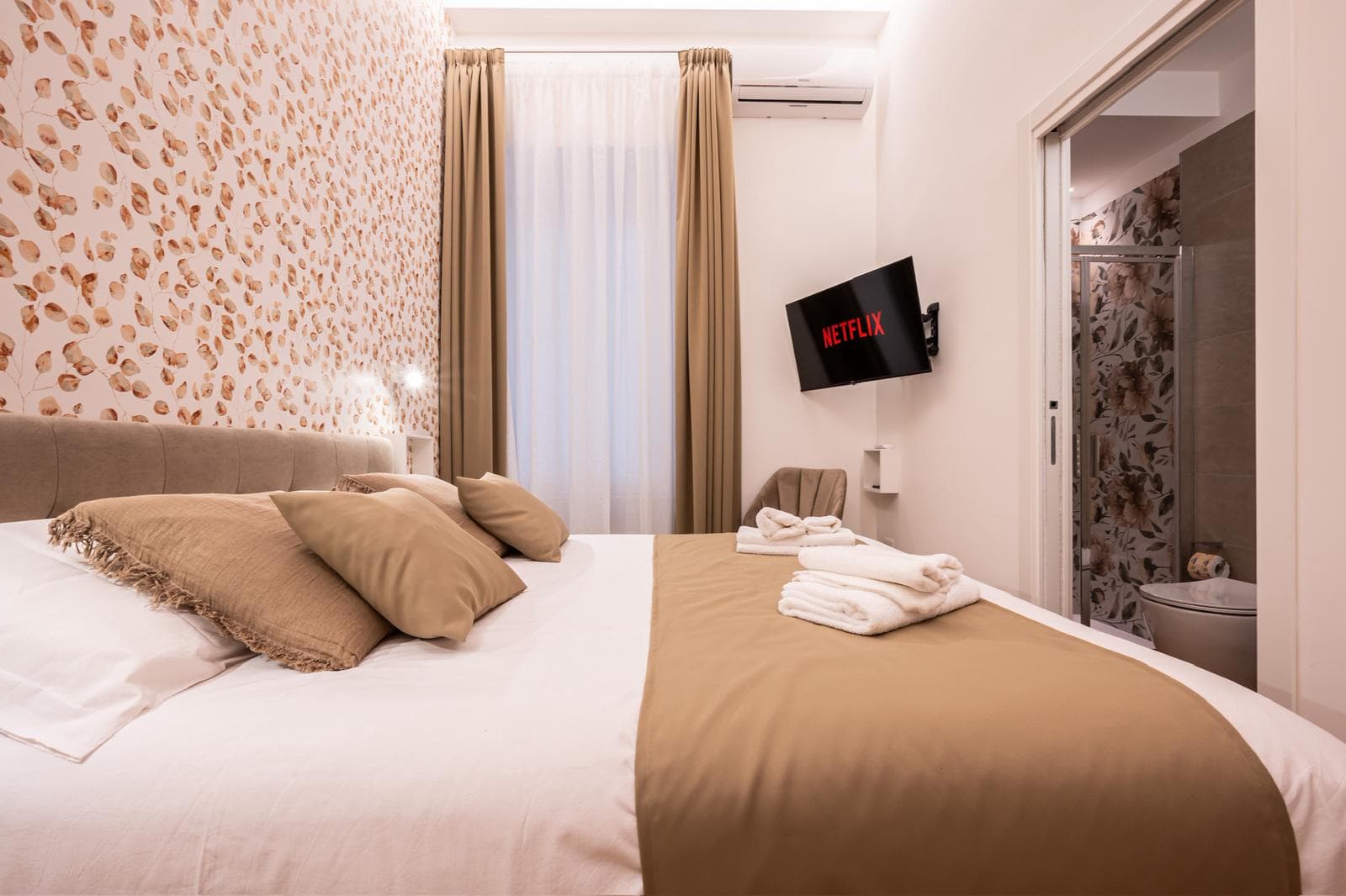 Modern bedroom with leaf-patterned wallpaper, a large bed, and a wall-mounted TV showing Netflix.